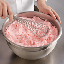 Pink colored Petits Fours butter creme in a bowl with a whisk