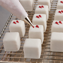 White layered mini cakes being hand decorated with red accents