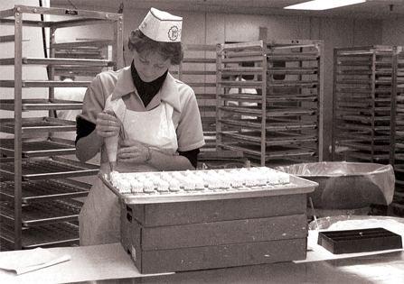 Women in 1960's in apron and hat hand decorating a tray of petits fours